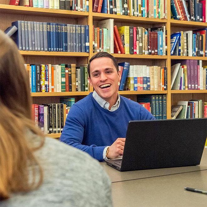 students sitting at a table with a professor discussing a religious book.